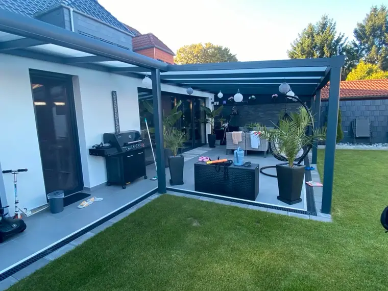 Anthrazitfarbene Terrassenüberdachung an einem weissen Neubau mit Rasenfläche