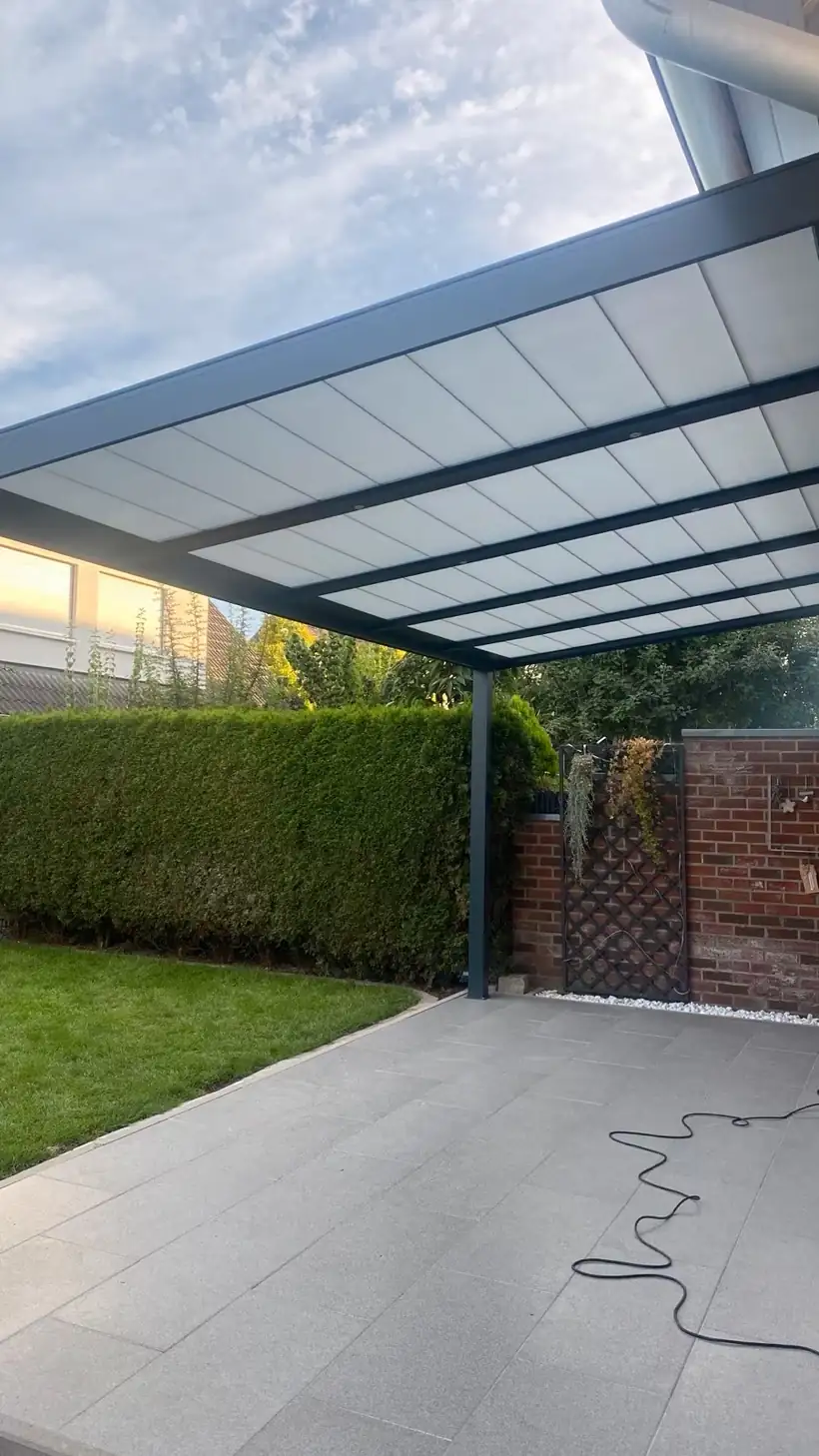 Am Abend fertig montierte Terrassenüberdachung aus Aluminium, warm beleuchtet, mit Baumaterial neben der Terrasse